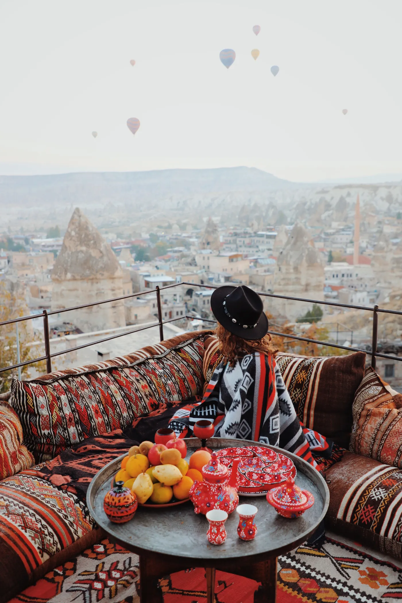 Terraço com tapetes e almofadas com vista para os balões da Capadócia